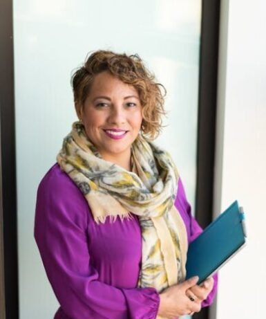 Smiling woman in a purple dress and scarf holding a tablet indoors.
